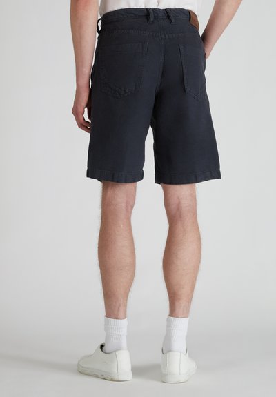 Shorts de algodón azul marino con un corte relajado, que presentan una cinturilla y dos bolsillos traseros. El dobladillo está vuelto hacia arriba y se llevan con zapatillas blancas.