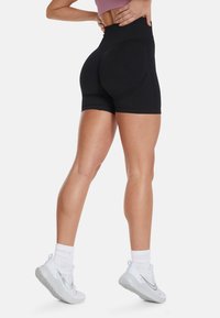 Black high-waisted shorts with a fitted design, textured detail at the back, and a smooth finish, paired with white athletic shoes.