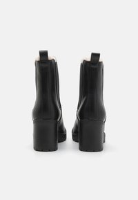 Botines de cuero negro con un tacón cuadrado texturizado, que cuentan con un forro suave visible en la parte superior y tiradores para facilitar su colocación.