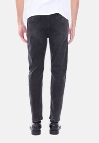 Pantaloni in denim neri con vestibilità slim, dotati di tasche posteriori e orlo pulito. Indossati con scarpe nere, visibili dalla vista posteriore.
