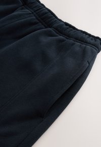 Dunkelblaue Jogginghosen aus weichem, strukturiertem Stoff. Ausgestattet mit einem elastischen Bund und seitlichen Taschen, zeichnet sich durch ein schlichtes Design und Nähte aus.