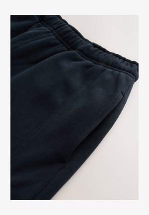 Pantaloni della tuta blu navy in tessuto morbido e strutturato. Presentano una cintura elastica e tasche laterali, con un design semplice e dettagli di cucitura.