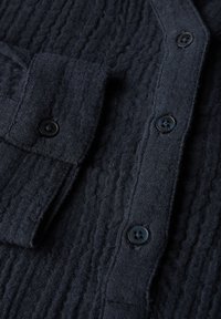 Cardigan in maglina a coste di colore blu navy, con chiusura a bottoni e dettaglio tasca sul lato sinistro. Bottoni neri in plastica.