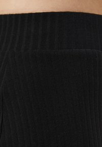 Black ribbed fabric, with a textured appearance, featuring a wide waistband and a snug fit, showcasing vertical ridges throughout.
