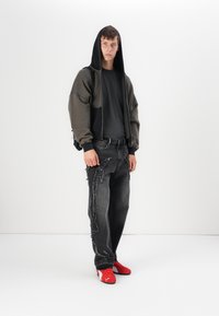 Hoodie oversized cinza escuro com mangas raglan sobre uma t-shirt preta, combinado com jeans pretos desgastados com detalhes em costura branca e ténis vermelhos.
