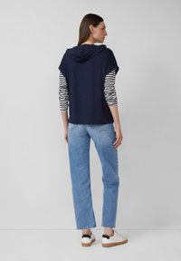 Marineblaues Hoodie mit gestreiften Ärmeln, kombiniert mit hellblauen geraden Jeans und weißen Sneakers mit schwarzen Akzenten.