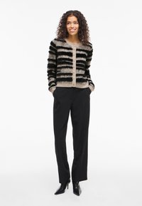 Cardigã riscado em preto e bege com uma textura felpuda, apresentando um colarinho redondo, botões frontais e punhos canelados, combinado com calças pretas.