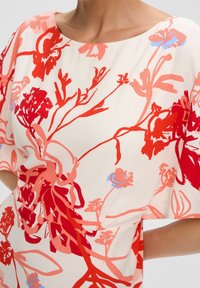 Blommig klänning med en krämfärgad bakgrund och djärva röda och rosa blommönster. Lätt passform, rund halsringning och flödande tyg.