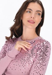 Roze gebreide trui met een geribbelde structuur en een overvloed aan pailletten in verschillende schaduwtonen van roze en zwart op de schouders.