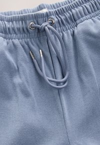 Jogging bleu clair en tissu texturé, avec taille élastique et cordon de serrage à extrémités métalliques pour réglage.