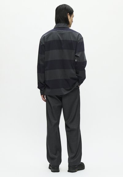 Donker gestreepte langemouwenshirt in marineblauw en grijs, gecombineerd met grijze wijde broek en zwarte schoenen, gezien vanuit de achterkant.