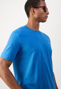 T-shirt de algodão azul com mangas curtas, gola redonda e um logótipo discreto no peito. Textura suave, design ajustado e cor sólida.