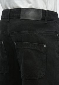 Czarne szorty z denimu z naszywką skórzaną na pasku, ozdobione guzikami oraz dwoma tylnymi kieszeniami z subtelnymi detalami szwów.