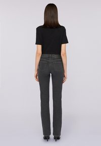 Camiseta negra de manga corta combinada con jeans de pierna recta de cintura alta en gris oscuro, que cuentan con cinco bolsillos y un parche de cuero en la cintura.