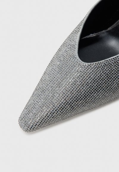 Hõbedane terava ninaga king, kaetud väikeste kristallidega, millel on sile must sisemus ja pehme tekstuur.