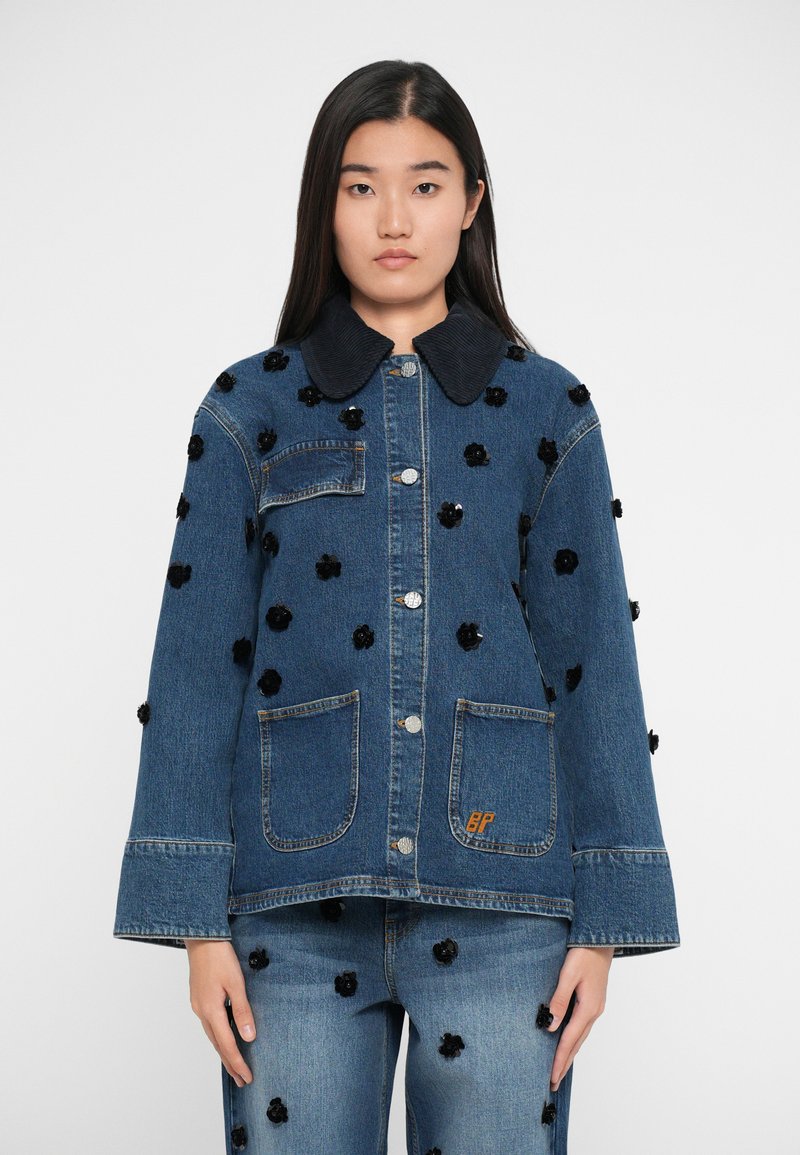 Jeans jakna z obrobljenim temnim žametnim ovratnikom, črnimi cvetličnimi aplikacijami, dvema sprednjima žepoma in majhnim oranžnim logotipom na robu.