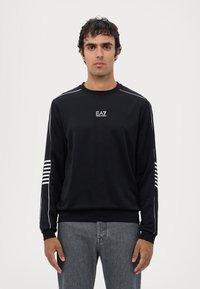 Felpa nera a maniche lunghe con logo EA7 bianco sul petto e strisce bianche sulle maniche. Il tessuto appare liscio; scollo rotondo; vestibilità comoda.