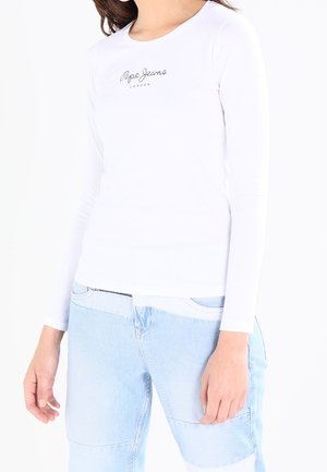 Kvinde iført en tætsiddende hvid langærmet top med teksten "Pepe Jeans London" og patchwork lyseblå denimjeans.