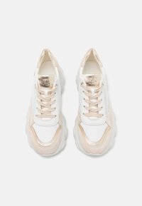 Hvite og beige joggesko med mesh-paneler, rund tå, tykk såle, metalliske detaljer på tungen og siden, og flate lisser.