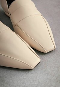 Mocassins en cuir beige à bouts pointus, avec une texture lisse et de subtils accents de couture sur la partie supérieure.