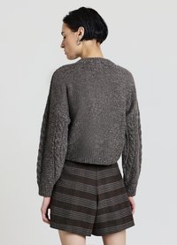 Grauer Strickpullover mit Zopfmusterärmeln, geripptem Saum und rundem Ausschnitt, kombiniert mit braunen karrierten Shorts mit grauen Streifen.