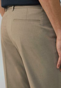 Beige maßgeschneiderte Hose mit glatter Textur, einer einzelnen Gesäßtasche und einem schlanken, geraden Schnitt.