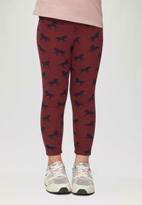 Bordowe legginsy z powtarzającym się wzorem niebieskich koni, elastyczny materiał i dopasowany krój, w połączeniu z szaro-białymi sneakersami.