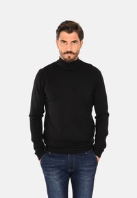 Maglione a dolcevita nero con una vestibilità aderente, colletto e polsini a costine. Abbinato a jeans in denim scuro. Texture liscia e design minimalista.