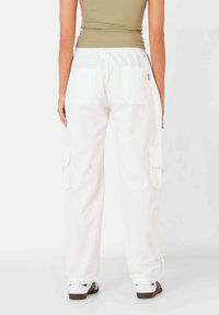 Witte cargobroek met een ontspannen pasvorm, zijzakken, elastische tailleband en drawstring manchetten. Gepaard met een aansluitend, olijfgroene top.