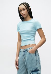 Világoskék bordázott rövid ujjú felső, testhezálló szabással, magasderekú, kopott hatású farmernadrággal, oldalzsebbel.