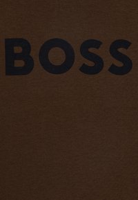 Hnědé bavlněné tričko s velkým černým nápisem "BOSS" uprostřed na přední straně, s hladkou texturou a jednoduchým designem.