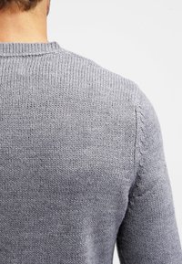 Maglione grigio lavorato a maglia con scollo rotondo e design delle spalle senza cuciture, caratterizzato da una texture morbida e un pattern di punto uniforme.