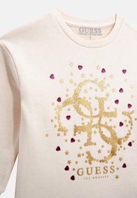 Felpa rosa chiaro con decorazioni a forma di cuore e stella in oro e burgundy. Presenta il logo "GUESS" sul fondo, collo rotondo e una texture morbida.