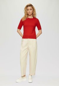 Maglietta a maniche corte rossa in maglia abbinata a pantaloni larghi beige; il modello indossa sneakers bianche con piattaforma. Design semplice senza motivi visibili.