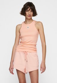 Perzikkleurig geribbeld tanktop met een ronde halslijn en een klein logo-embleem; gecombineerd met bijpassende short met koordjes van een zachte textuur.