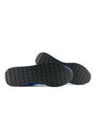 Suole di scarpe in gomma nera con modelli di battistrada esagonali, con accenti blu lungo i bordi. Le suole sono lisce e piatte.