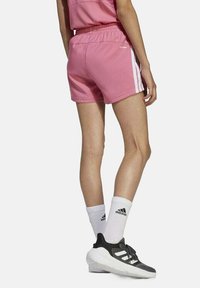 Bermudas deportivas rosas con una cinturilla elástica y franjas blancas a los lados, combinadas con zapatillas negras y calcetas blancas. 