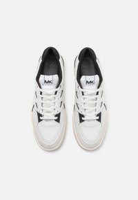 White sneakers with black accents and laces. Smooth leather and rubber outsole, featuring perforations and prominent "MK" logo on the tongue.