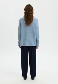 Jasnoniebieski, oversize'owy sweter o dzianinowej fakturze z prążkowanym wykończeniem, zestawiony z ciemnoniebieskimi spodniami o szerokich nogawkach, prezentującymi luźny krój.