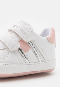 Białe skórzane buty z różowymi akcentami i srebrnymi paskami. Posiadają rzepy oraz teksturowany detal z boku. Zaokrąglony kształt noska.