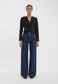 Blazer noir ajust é avec un col en V, cinq boutons et manches longues, associé à un jean en denim foncé à jambes larges et des chaussures marron.