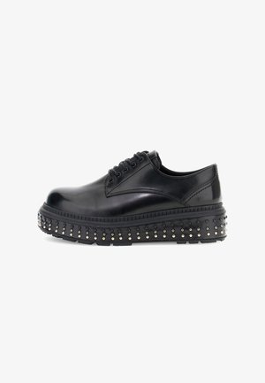 Scarpa platform nera in pelle con lacci e dettagli di borchie attorno alla suola spessa, mostrata in profilo laterale su sfondo bianco.