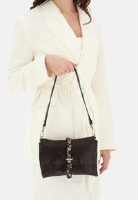 Borsa a mano in pelle nera con finitura testurizzata, dotata di una chiusura decorativa con accenti metallici e di una tracolla removibile.