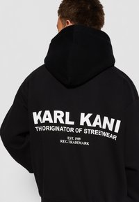 Black hoodie featuring a large white logo text on the back, reading "KARL KANI THE ORIGINATOR OF STREETWEAR" with established year 1989.