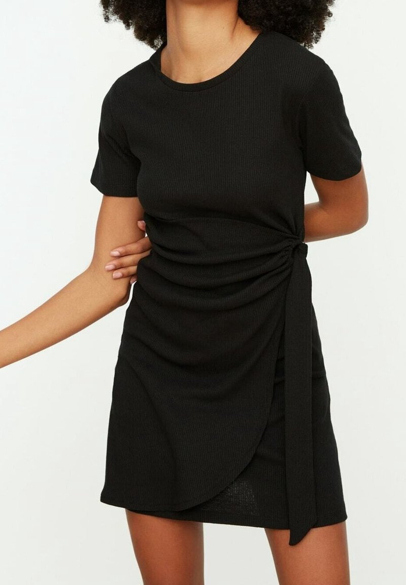 Robe noire à côtes avec manches courtes, présentant un détail twisté sur le côté et un nœud à la taille pour une silhouette ajustée.
