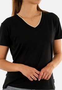 T-shirt nera a maniche corte con scollo a V, caratterizzata da un bordo beige a contrasto lungo il collo e una vestibilità comoda. Tessuto morbido e design semplice.