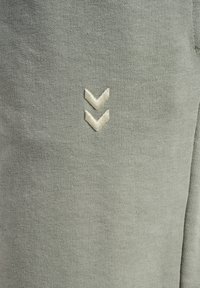 Ljusgrön sweatshirttyg med en stickad textur; har en krämfärgad broderad logotyp av två nedåtriktade chevrons på framsidan.