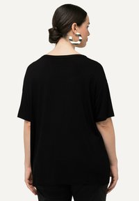 Camiseta negra de gran tamaño hecha de tela suave, con un ajuste holgado, mangas cortas y un escote ancho. Textura suave sin patrones.