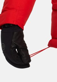Guanto in pelle nera che stringe un cordone rosso, attaccato a una manica rossa e testurizzata. Il guanto presenta un logo nella zona del polso.