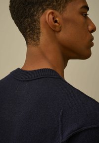 Maglione lavorato a maglia di colore navy con scollatura rotonda, tessuto strutturato e orlo a costine. Mostra la vista posteriore con dettagli di cucitura minimi vicino al colletto.